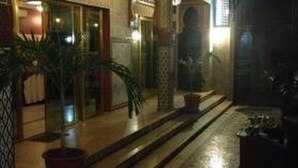 A dimly lit indoor area with a tiled floor, potted plants, and a doorway leading to another room. - Hotel Cabourg (Dakar)