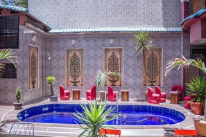 A pool area with tiled walls, red chairs, and potted plants. - Hotel Cabourg (Dakar)