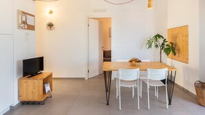 A modern dining area with a wooden table, white chairs, a television on a wooden cabinet, and a plant on the table.