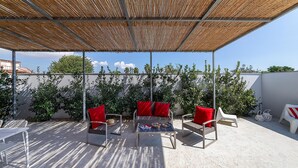 An outdoor patio with a bamboo canopy, two wicker chairs with red cushions, a small table, and a white chair.