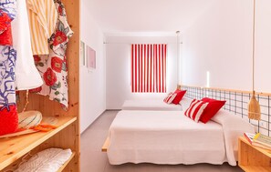 Two beds with white bedding and red pillows, a wooden headboard, and a wardrobe with a floral-patterned cloth.