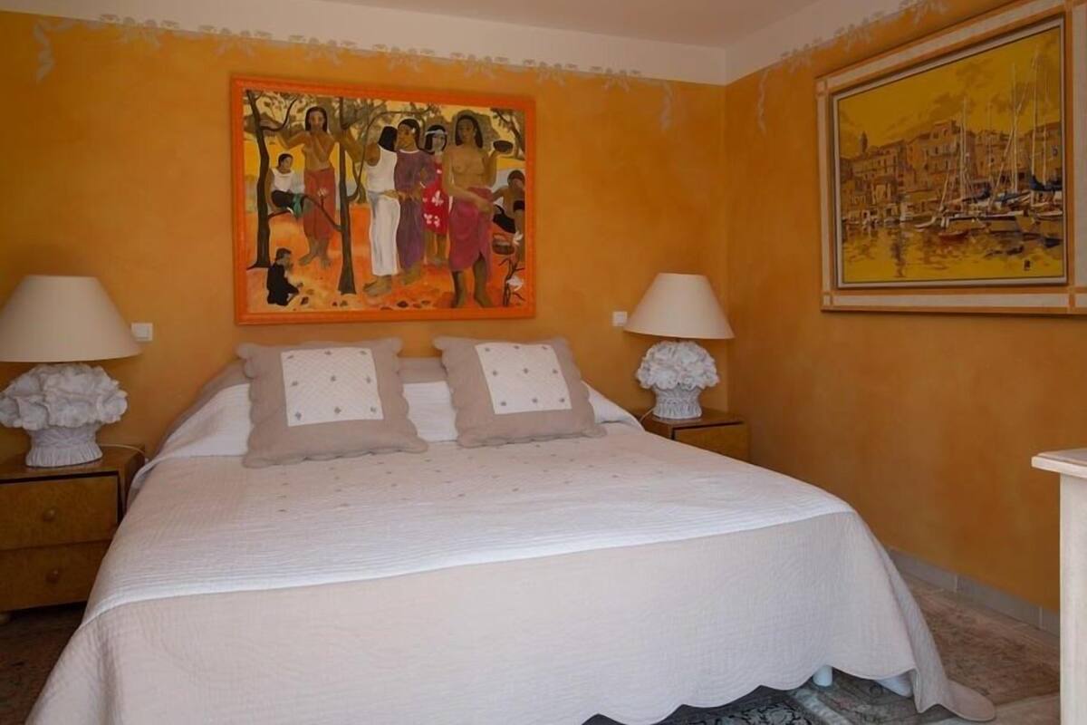 Un dormitorio con una cama, dos mesitas de noche, dos lámparas y dos cuadros en las paredes.