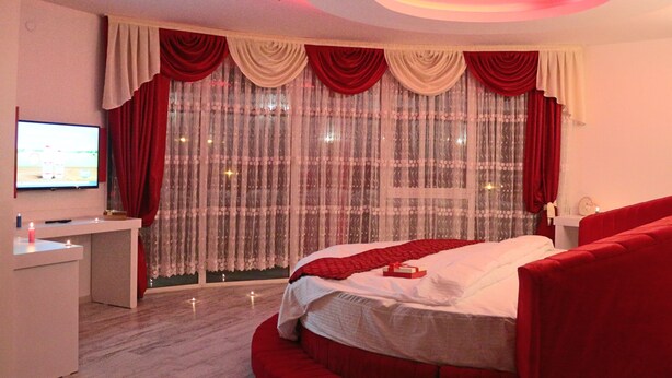 A bedroom with a bed, a television, a desk, and a window with curtains. - Grand Beyaz Saray Hotel (Duzce)