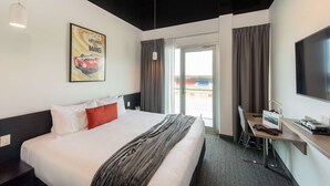 A hotel room with a bed, a desk, a chair, a TV, and a window with curtains.