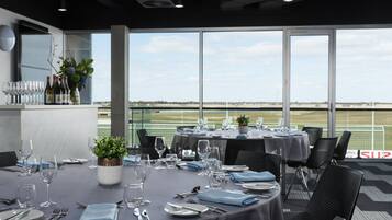 Un restaurante con mesas dispuestas para comer, un centro de mesa con plantas y vistas a un campo deportivo a través de amplios ventanales.