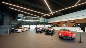 A modern building interior with a reception desk, a staircase, and several classic cars on display.