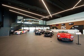 A modern building interior with a reception desk, a staircase, and several classic cars on display.