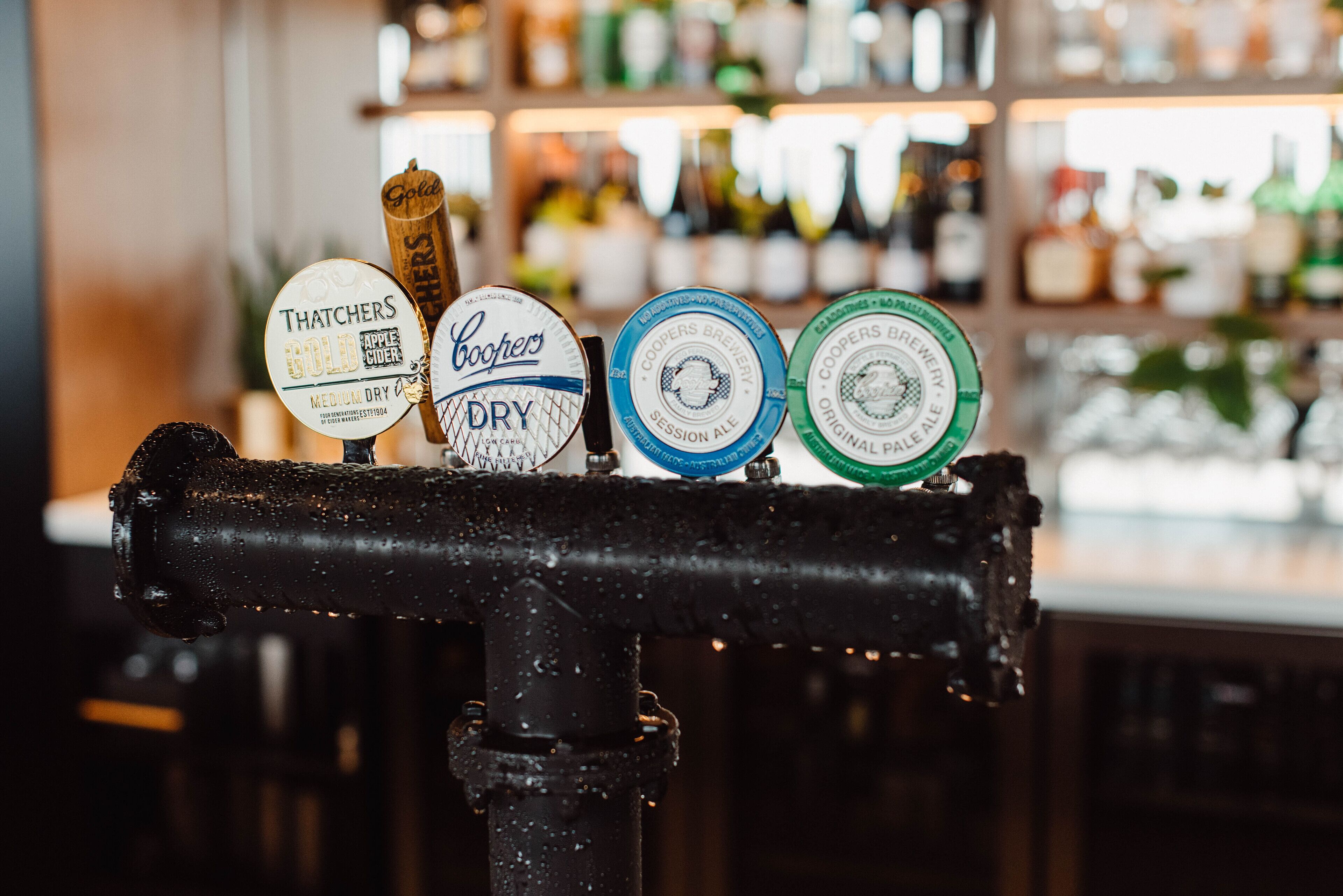 A tap with various beer labels, including brands like Coopers and Thatchers, in a bar setting.