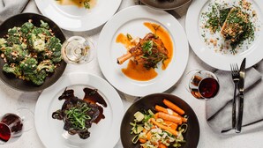 A variety of dishes on plates, including steak, vegetables, and seafood, arranged on a table with cutlery and glasses.