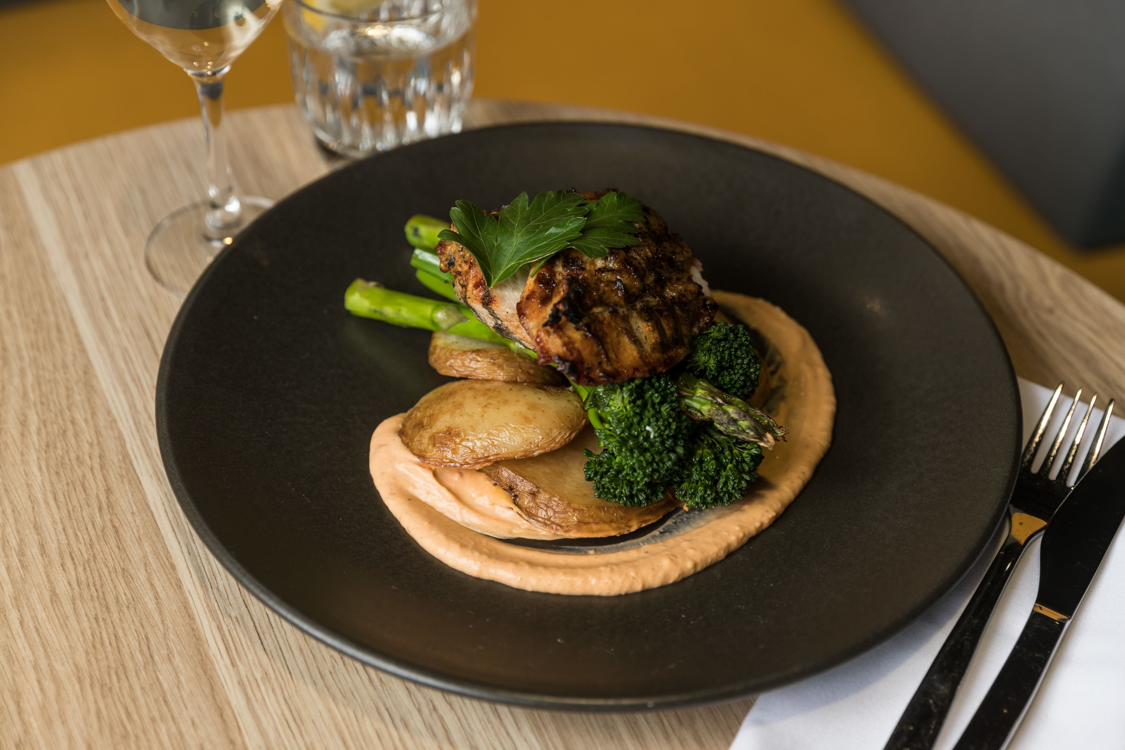 A plate of food with a piece of meat, broccoli, and potatoes on a black plate.