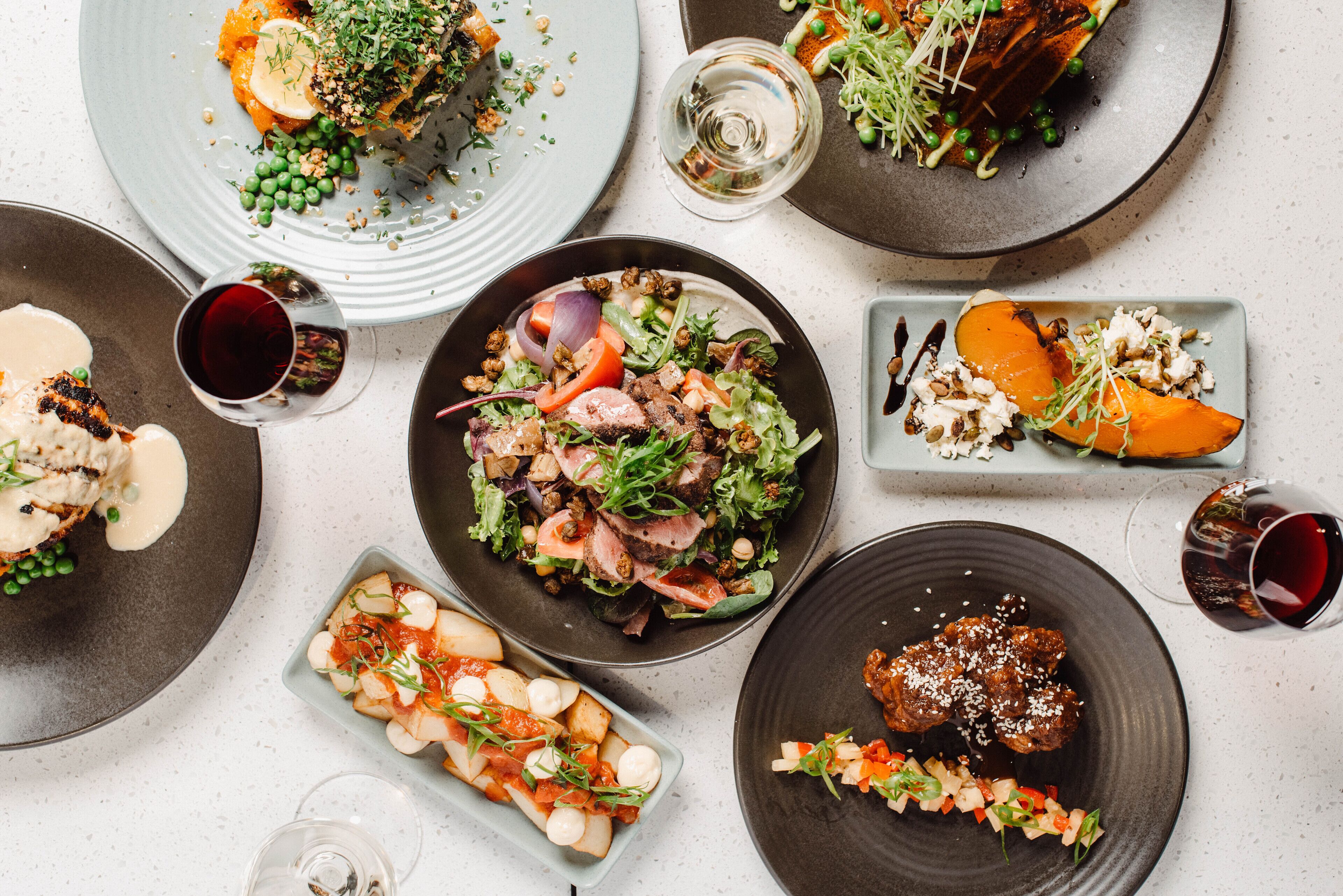 A variety of dishes on plates, including salads, meats, and vegetables, with glasses of red wine.
