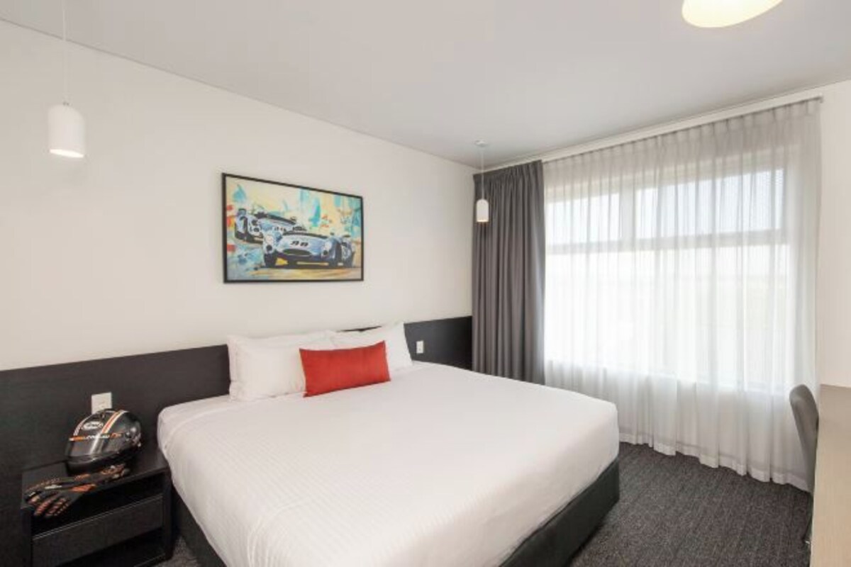 A hotel room with a large bed, a nightstand, a painting, and a window with curtains.
