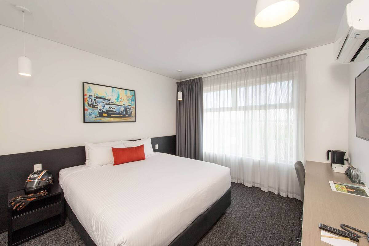 A hotel room with a large bed, a desk with a chair, a television, and a painting on the wall.
