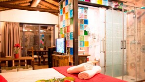 A hotel room with a bed, a TV, a shower, and a glass door with colorful tiles. - Casa Rural El Cuco (Solosancho)