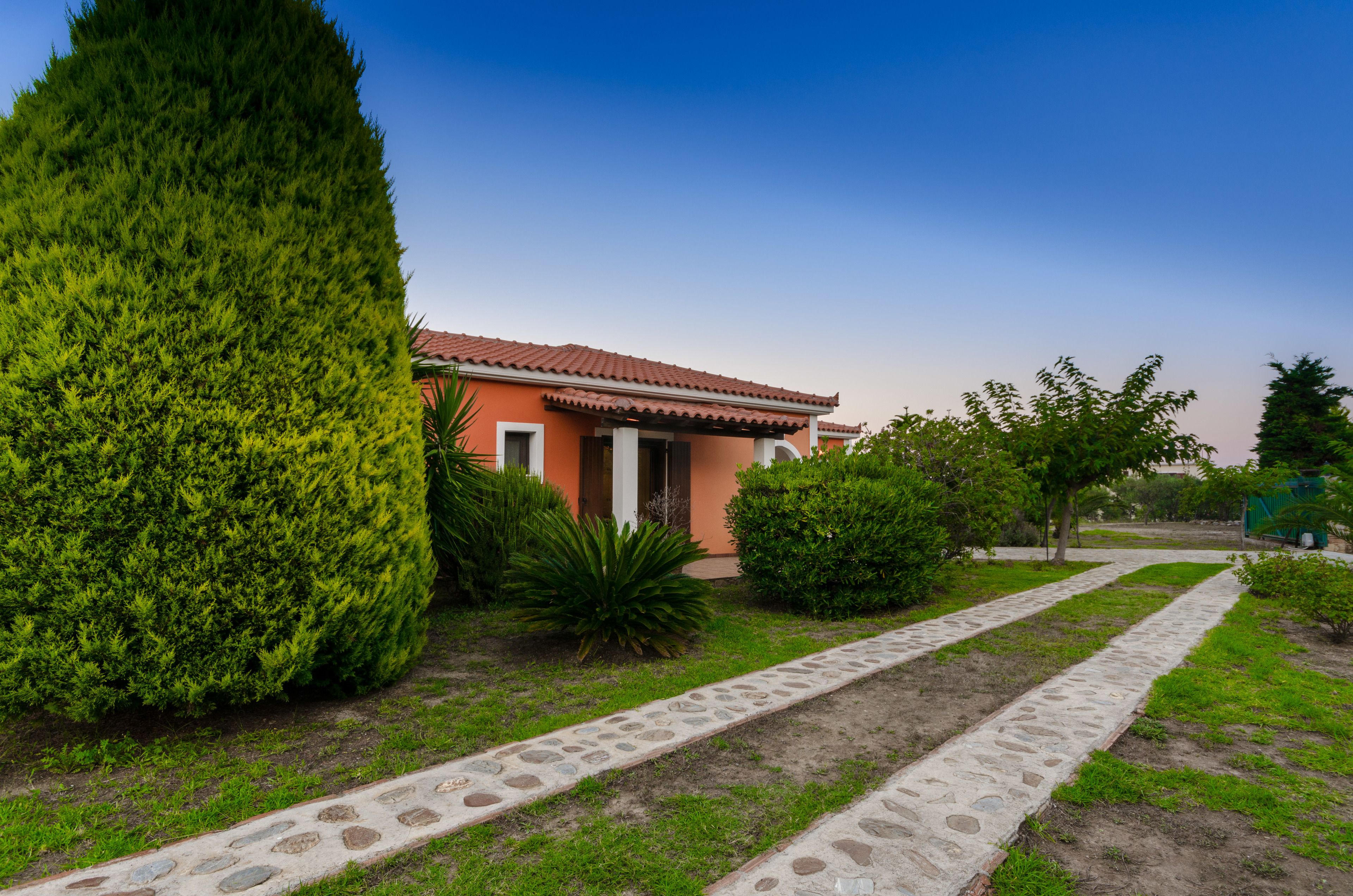 Una casa con techo rojo, rodeada por un camino de piedra y vegetación.