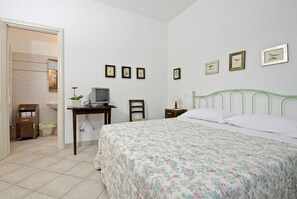 A bedroom with a bed, a desk with a computer, a chair, a nightstand, and framed pictures on the wall. - Agriturismo Il Sambuco (Monteriggioni)