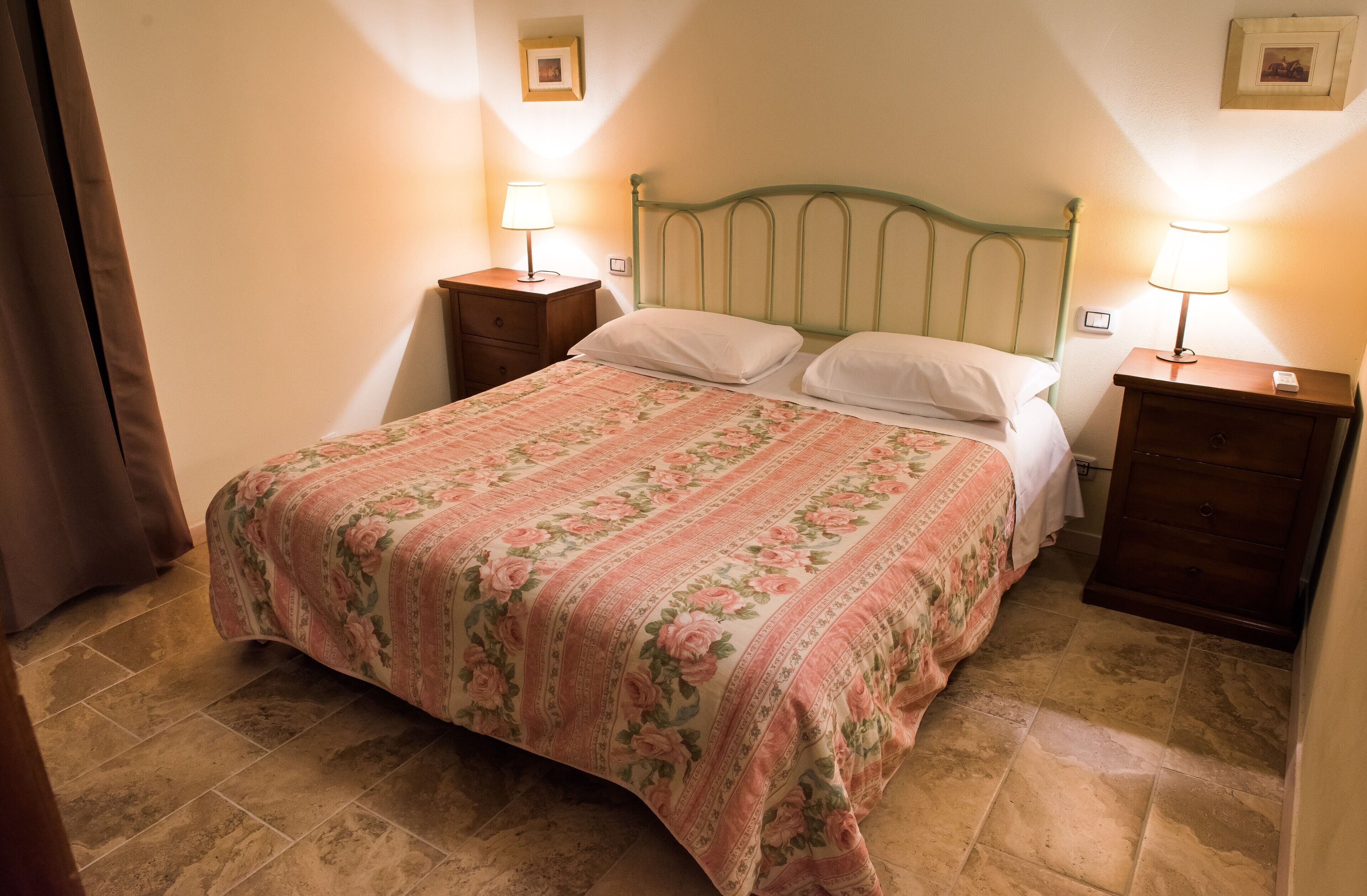 Una cama bien hecha con una colcha estampada, dos mesitas de noche con lámparas y un marco de fotos en la pared.