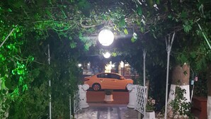 A paved pathway leading to a parked car under a canopy of trees, with a lamp post and potted plants along the sides. - Tecimen Hotel (Kusadasi)