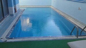 An indoor swimming pool with clear blue water, a tiled floor, and a green artificial turf area. - Tecimen Hotel (Kusadasi)