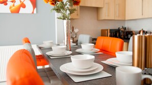 A modern kitchen with a dining area. It includes a kitchen counter, a dining table set with white plates and bowls, and a vase with orange flowers. - ByEvo 1 Brabloch GLA Apartment  (Paisley)