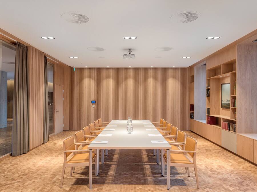 A conference room with a long table, chairs, and a bookshelf with books and decorative items.