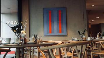 A modern cafe interior with wooden chairs and tables, a large abstract painting on the wall, and a window with a view.