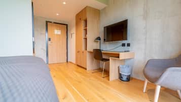 Ein Zimmer mit einem Bett, einem Schreibtisch mit Stuhl, einem Fernseher und einem Papierkorb.