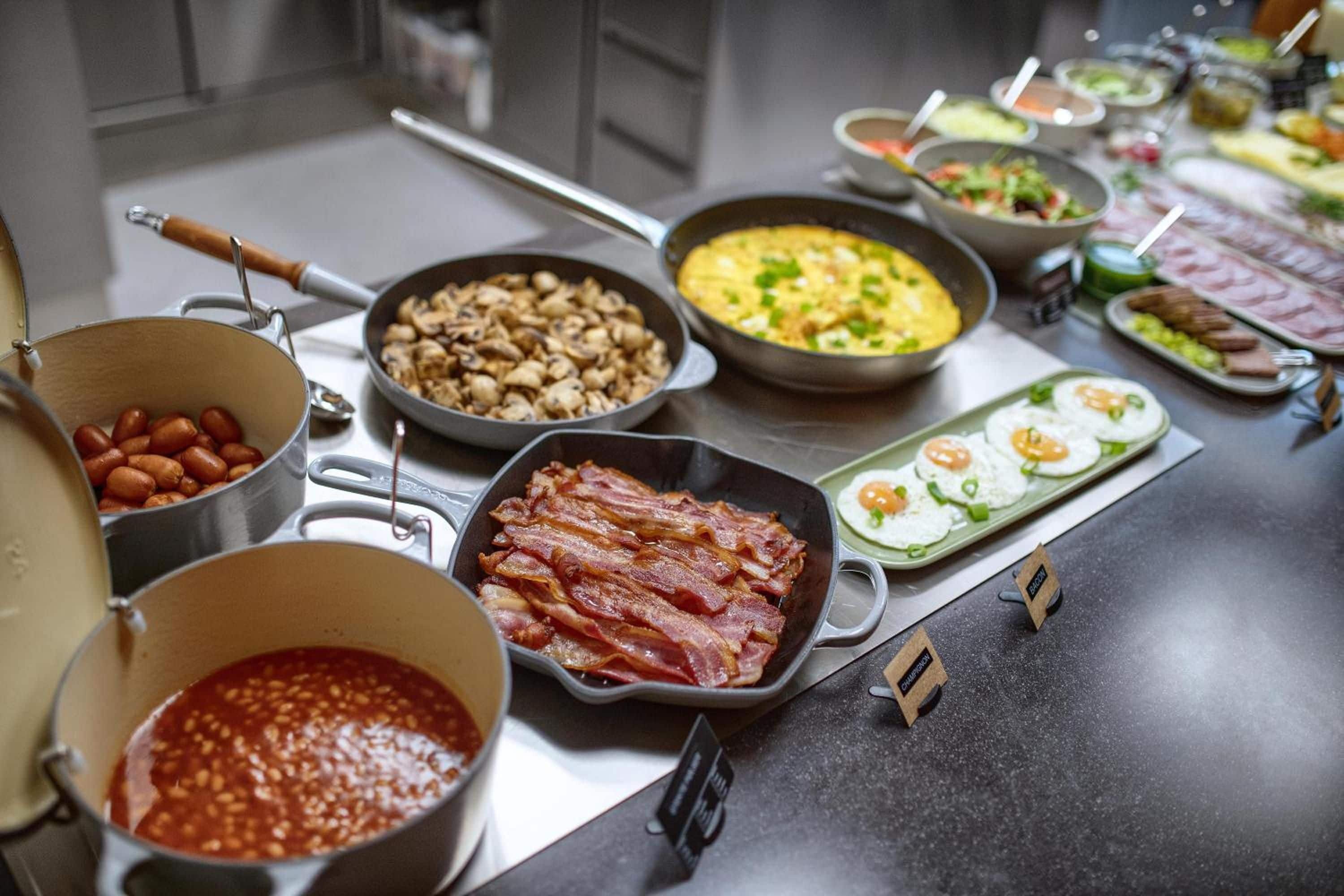 A buffet with various dishes including bacon, mushrooms, and eggs.