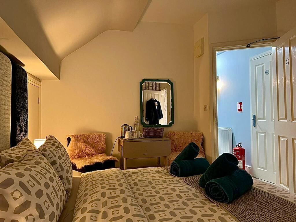 Quarto de hotel com uma cama, cômoda, espelho e porta que dá para outro quarto.