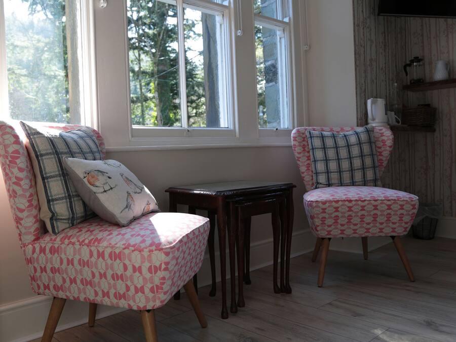 Een kamer met twee gestreepte stoelen, een klein tafeltje en een raam met uitzicht op bomen.