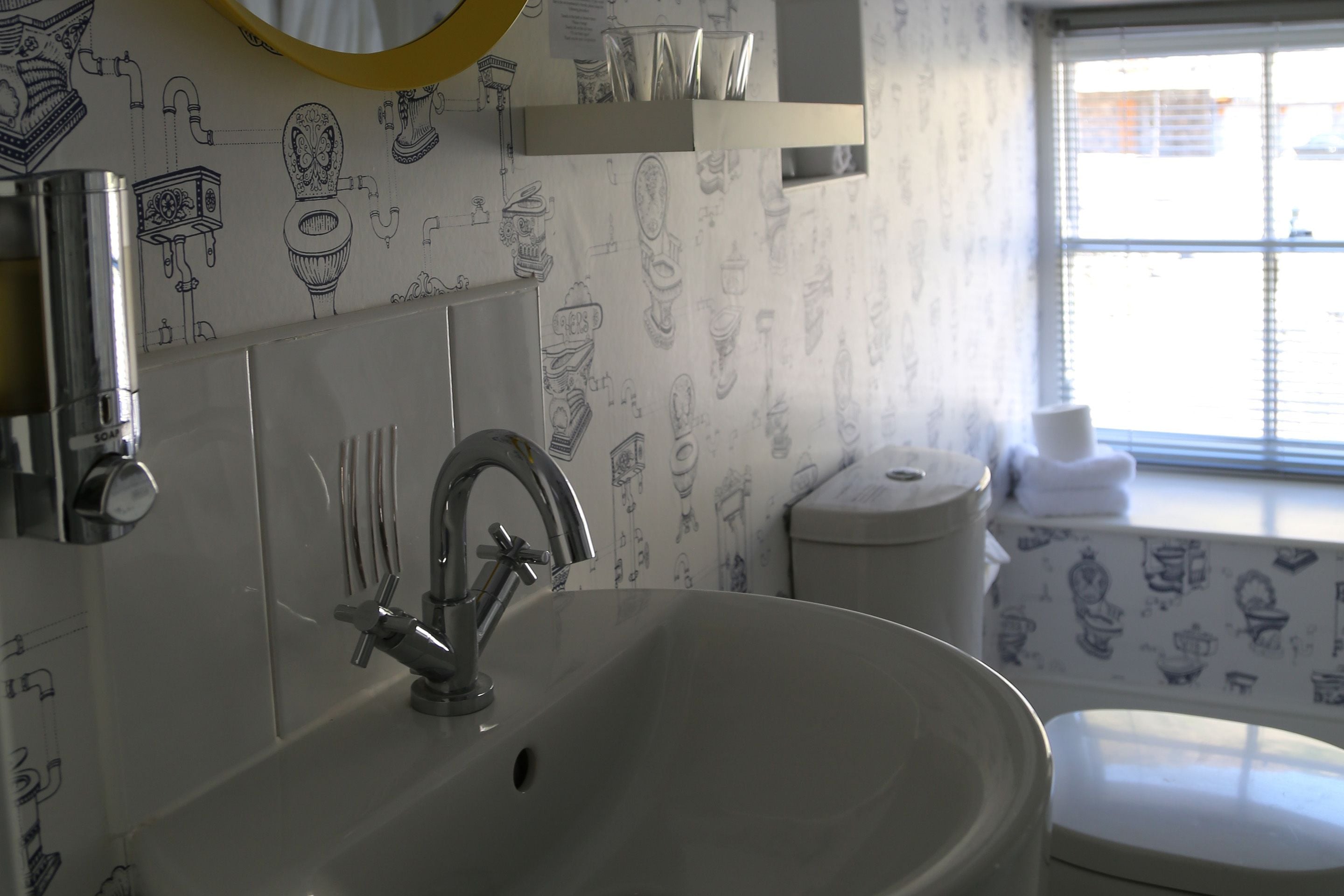 A bathroom with a white sink, a mirror, and a toilet. The walls have a pattern of various bathroom fixtures.