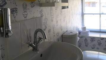 A bathroom with a white sink, a mirror, and a toilet. The walls have a pattern of various bathroom fixtures.