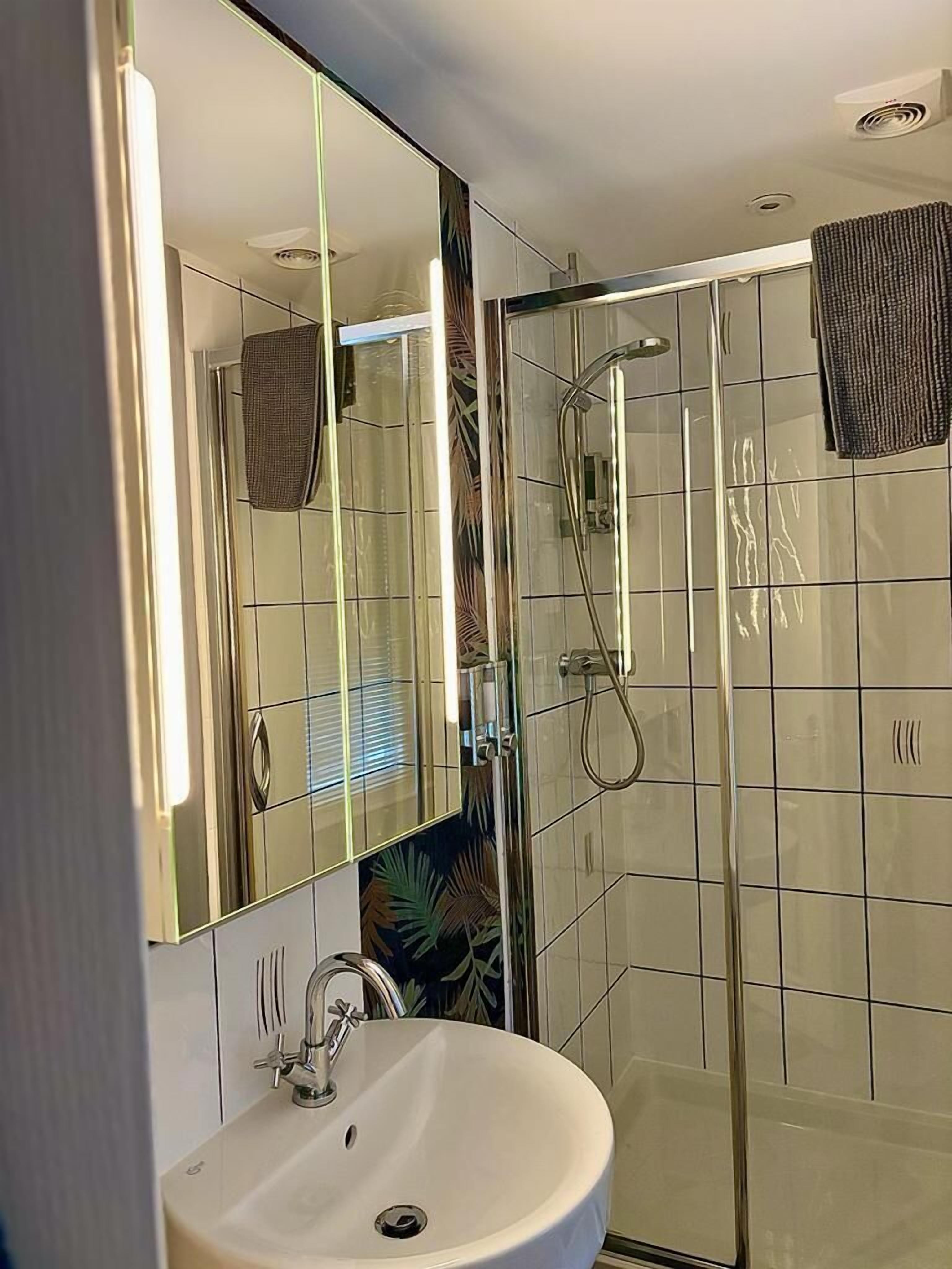 Un baño moderno con ducha de mampara de vidrio, lavamanos con espejo y paredes con azulejos.
