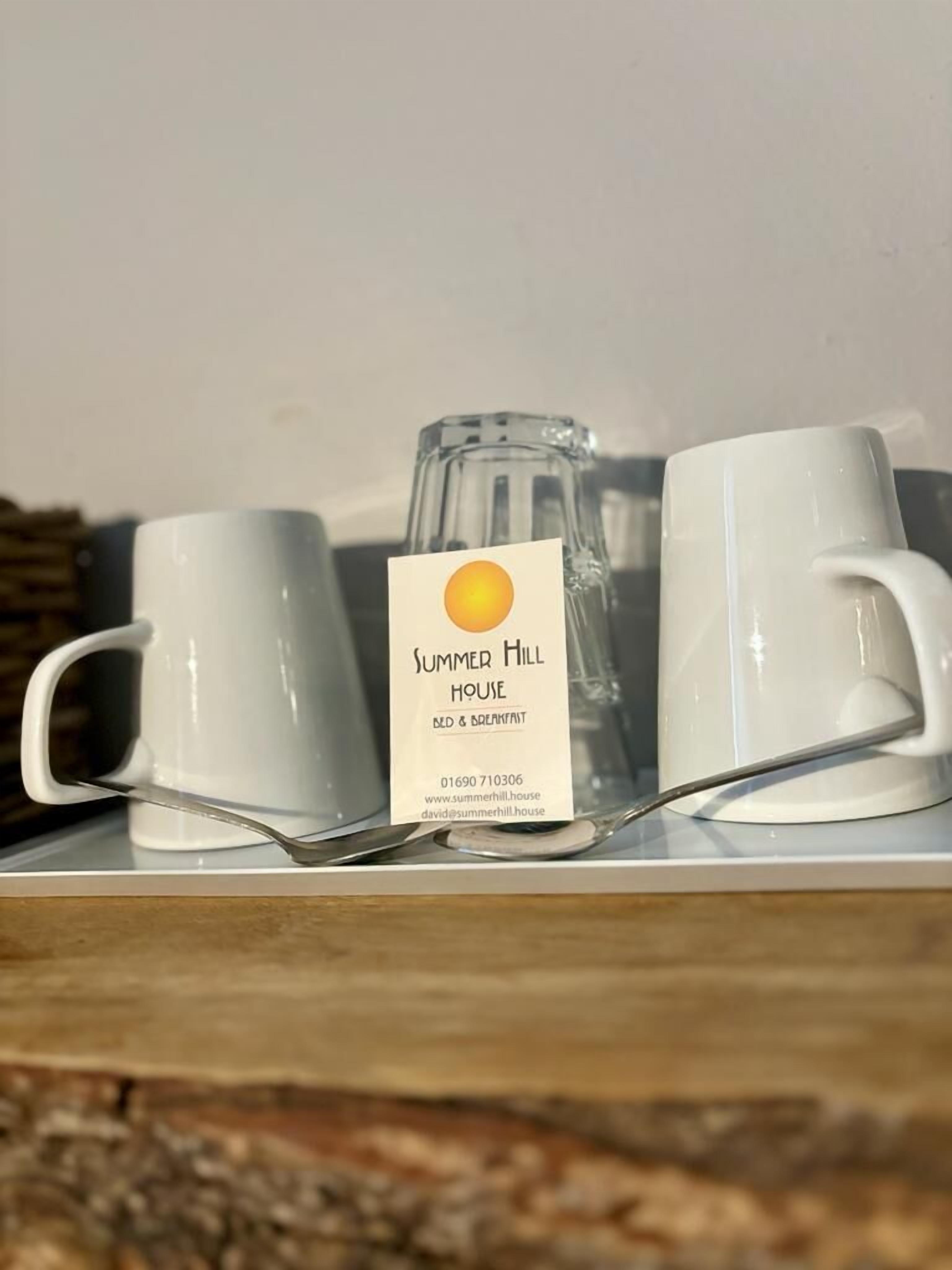 A white mug, a glass pitcher, and a sign for Summer Hill House Bed & Breakfast.