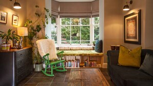Een knus hoekje om te lezen, met een bankje, boekenkasten en uitzicht op groen buiten.