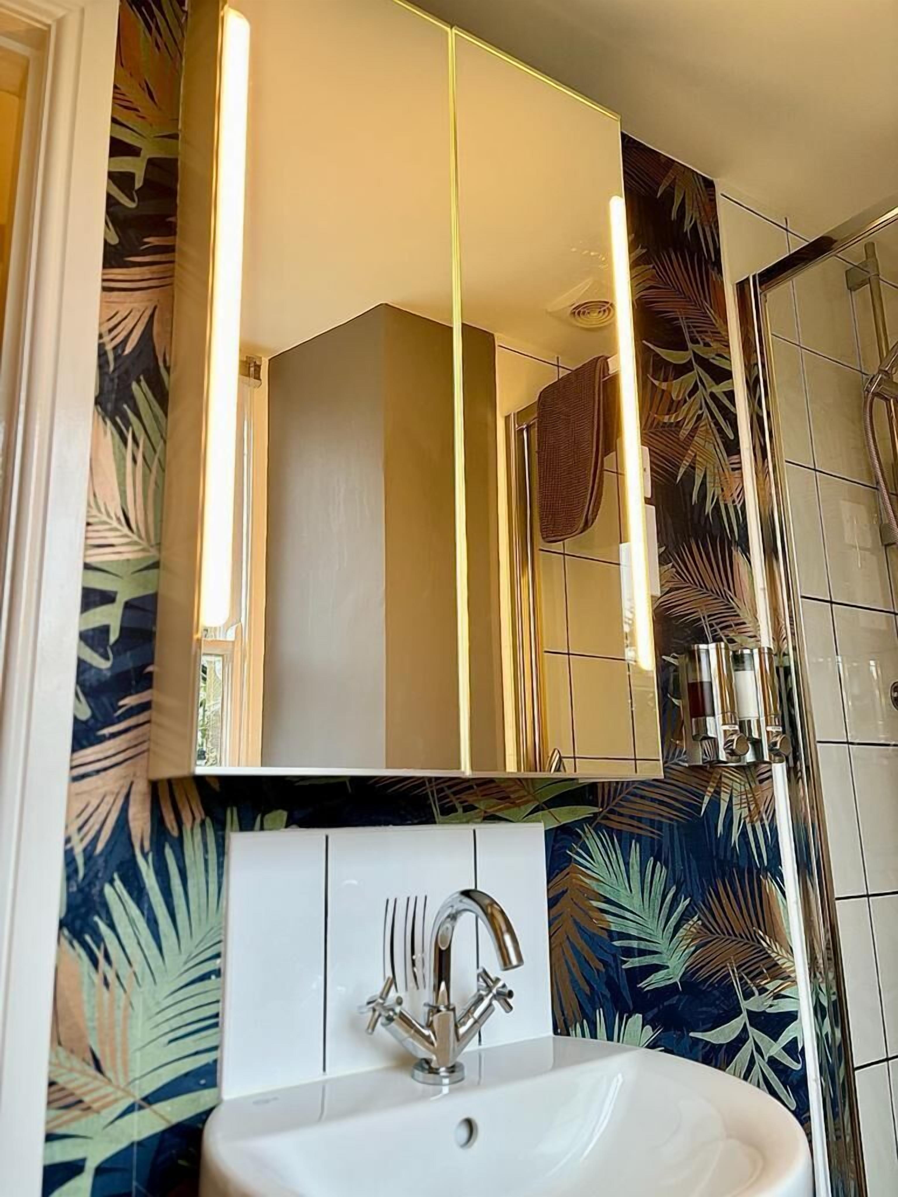 Een badkamer met een witte wastafel, een grote spiegel en een douchegedeelte.