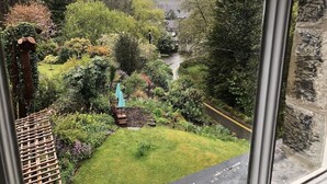 Een tuin met een houten terras, een bankje en uitzicht op een rivier en huizen in de verte.