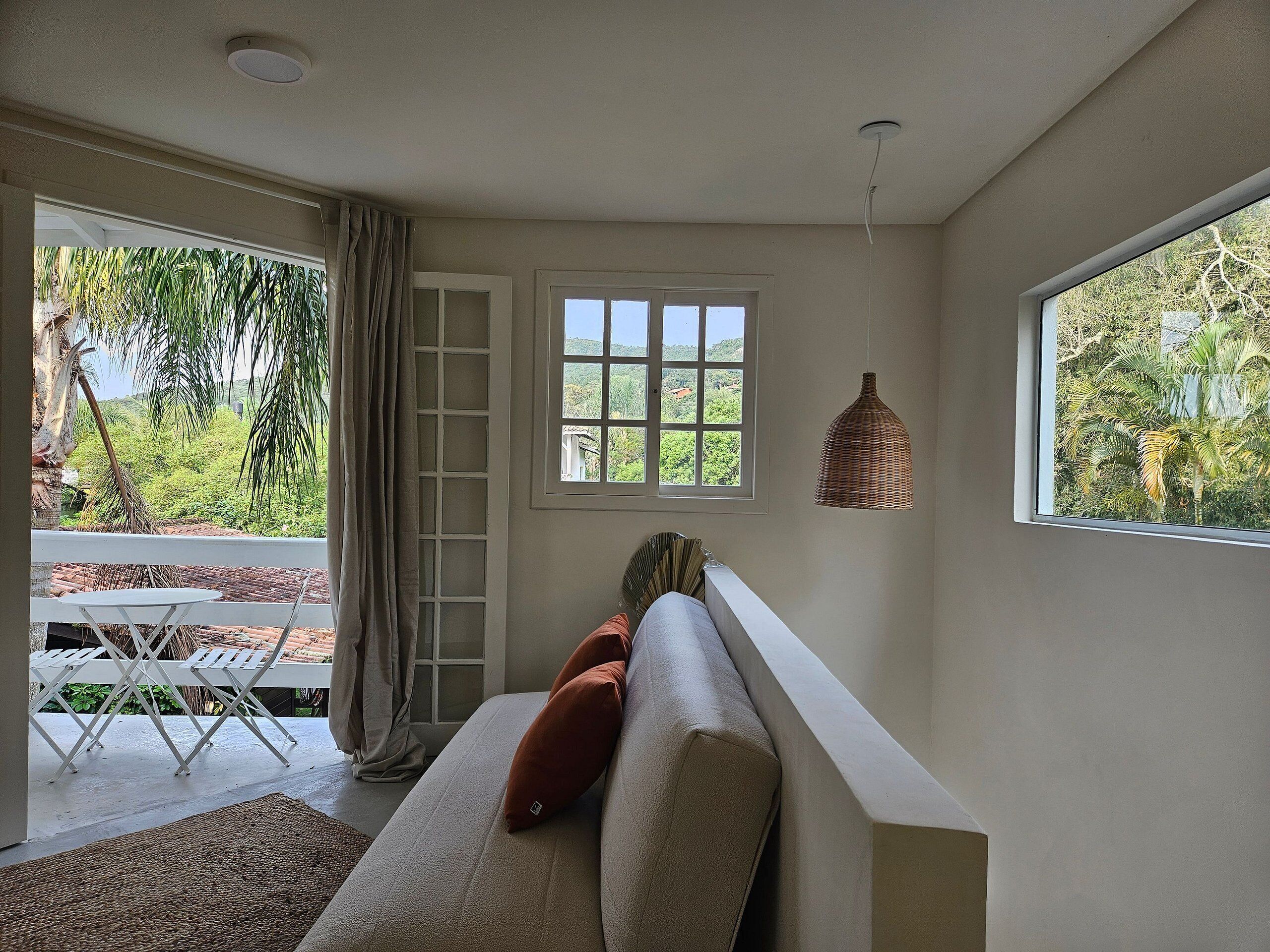 A room with a sofa, a window, and a view of greenery outside.