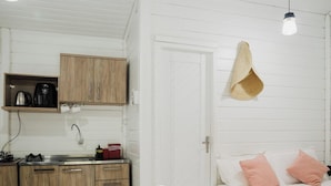 A compact room with a kitchenette, a bed with pink pillows, and a hanging light fixture. - Quinta da Margem (Florianópolis)
