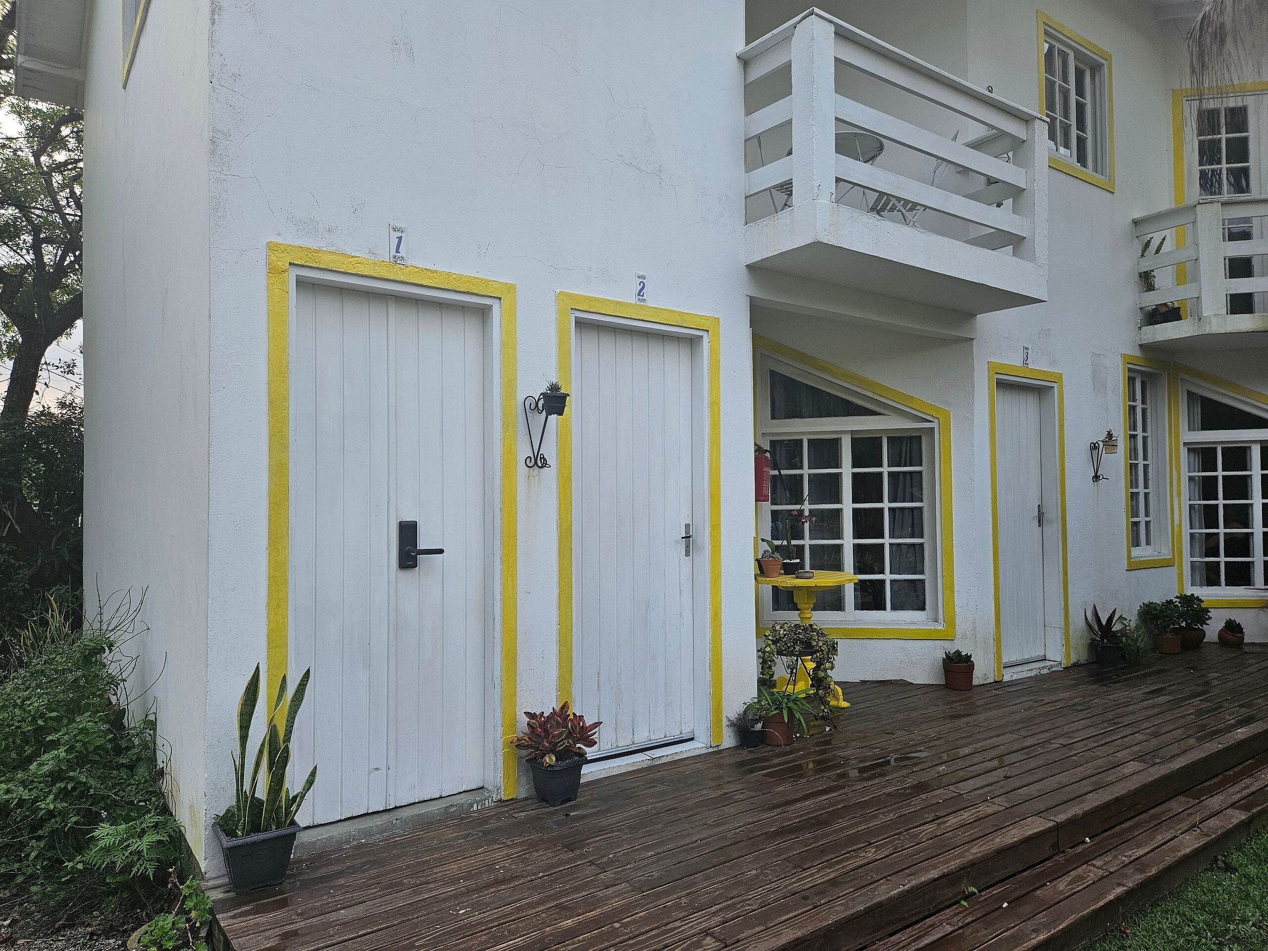 A building with two white doors with yellow trim, a balcony, and potted plants on the porch.