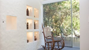 A room with a wicker rocking chair, a glass door leading outside, and shelves with decorative items. - Quinta da Margem (Florianópolis)