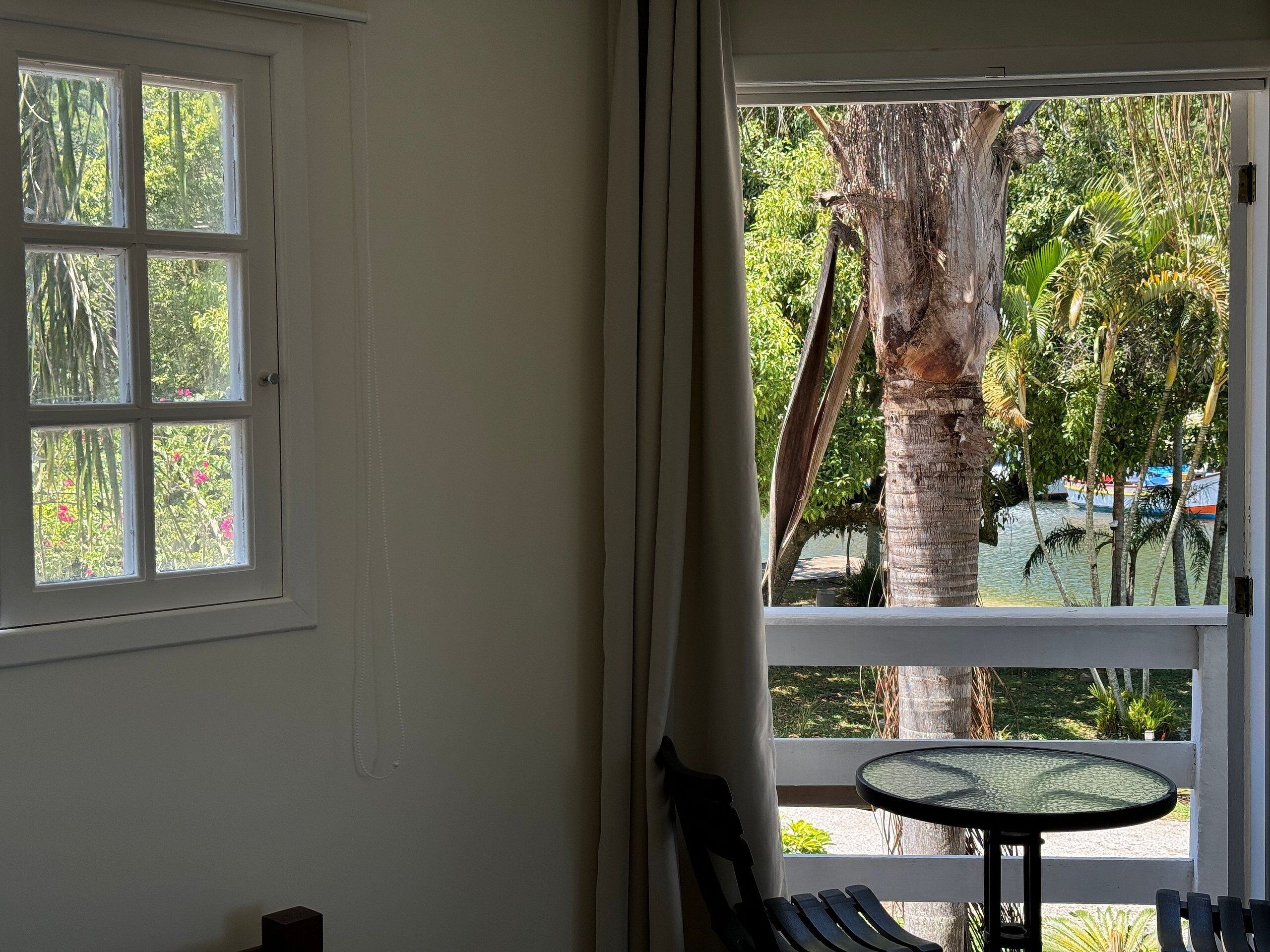 Quarto com uma janela grande, uma mesa pequena e um banco.