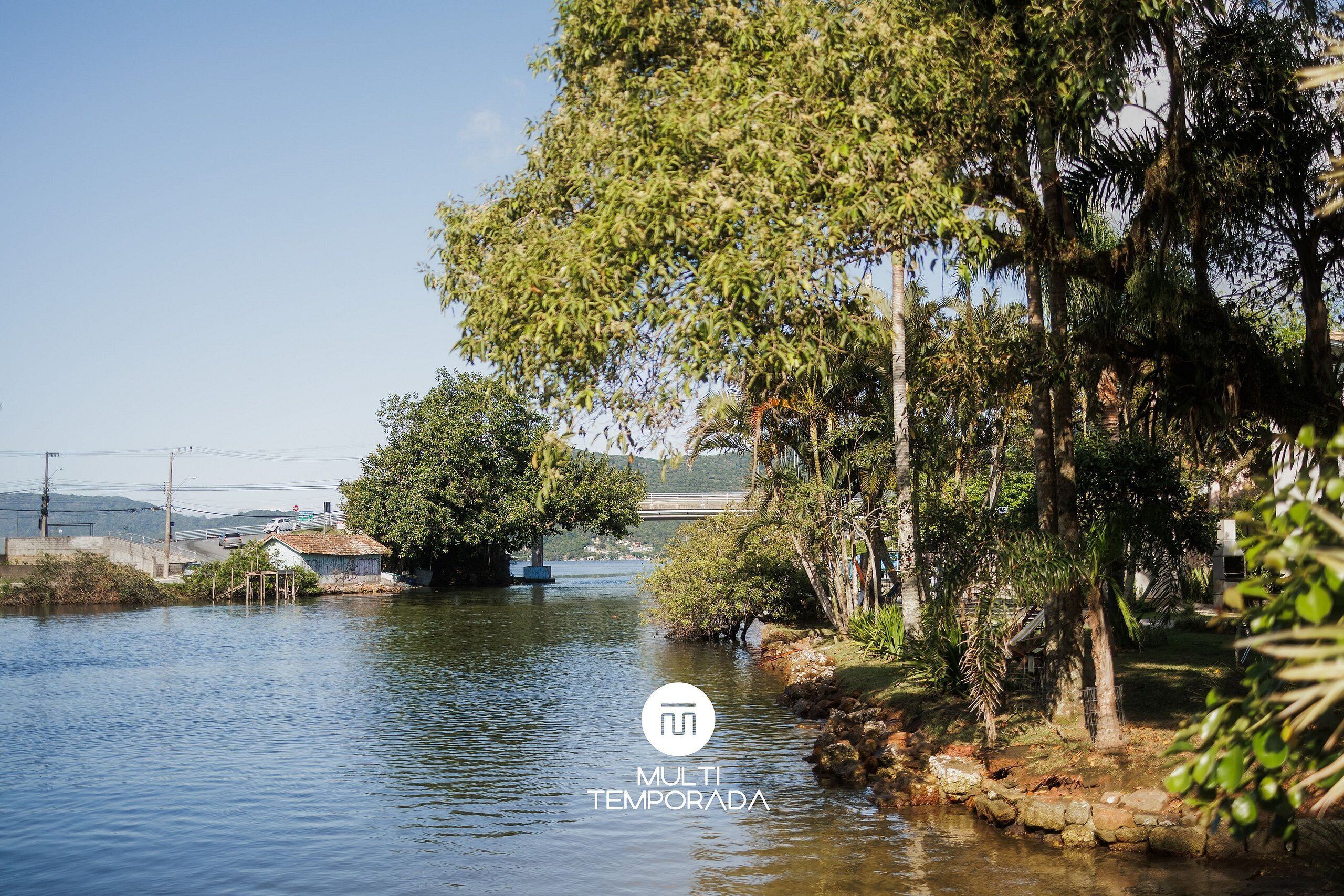 A calm river with a small house on the left and lush greenery on the right.