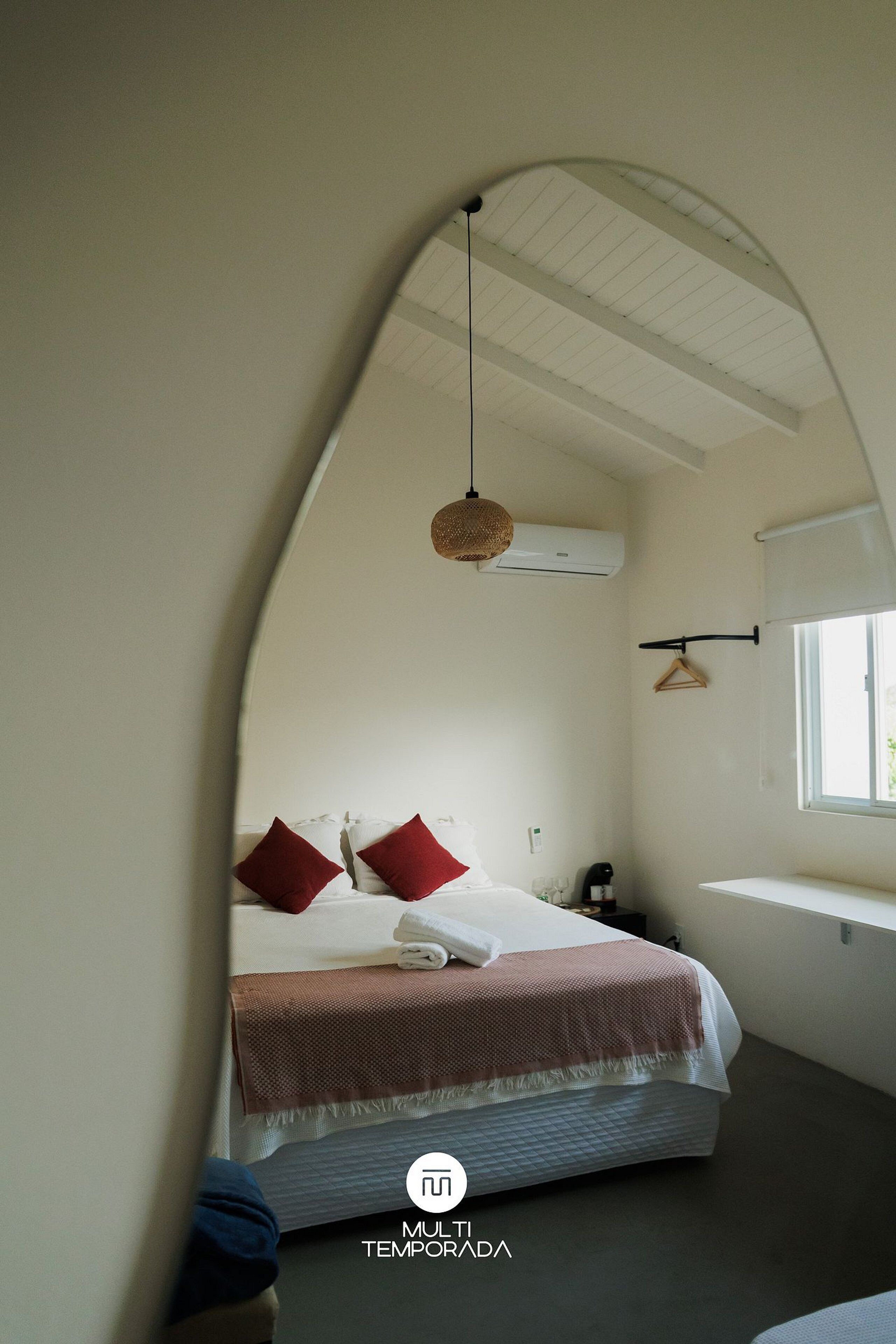 Une chambre à coucher avec un lit, des oreillers, un luminaire suspendu, une fenêtre et un appareil de climatisation.