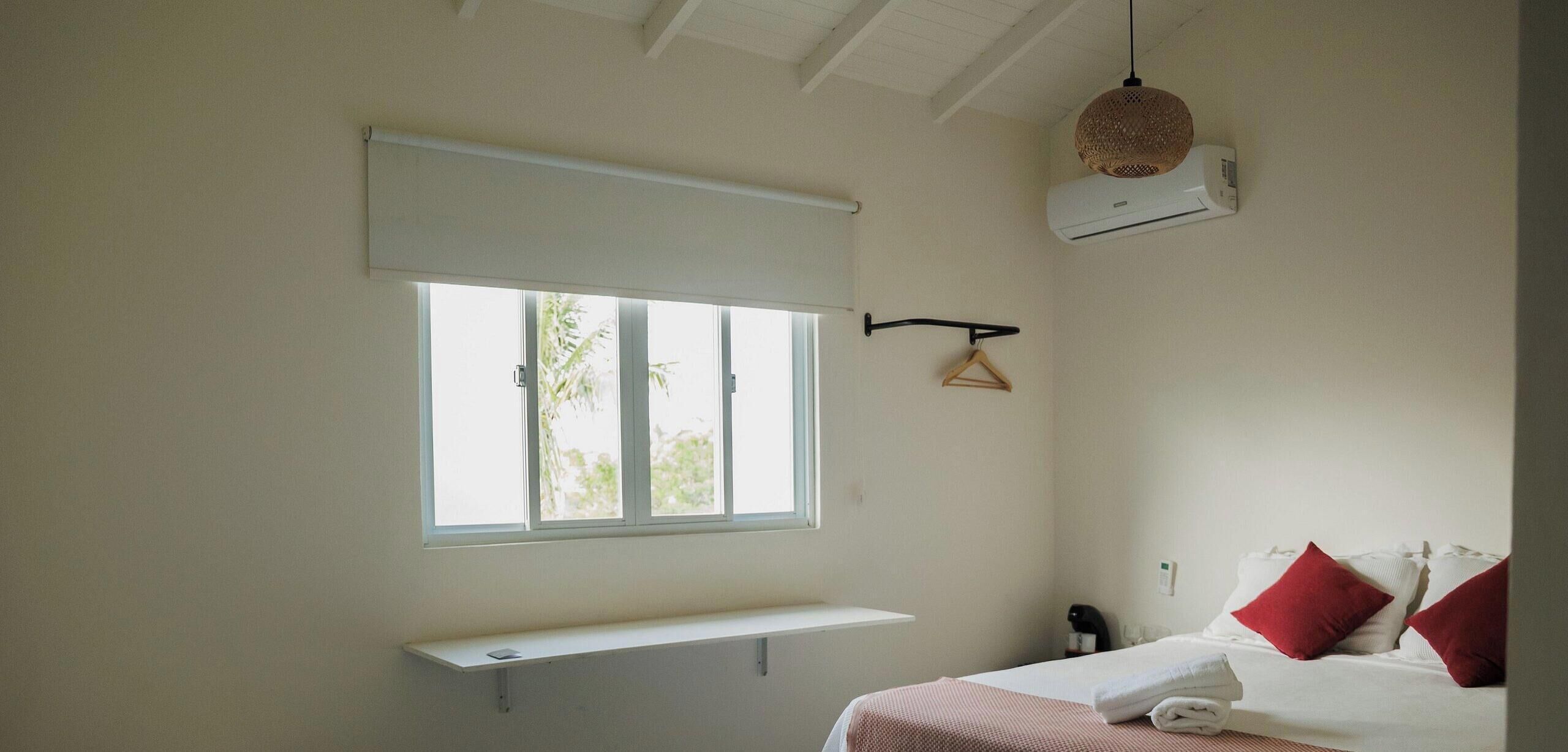 Une chambre à coucher avec un lit, une fenêtre, un luminaire suspendu et un climatiseur fixé au mur.