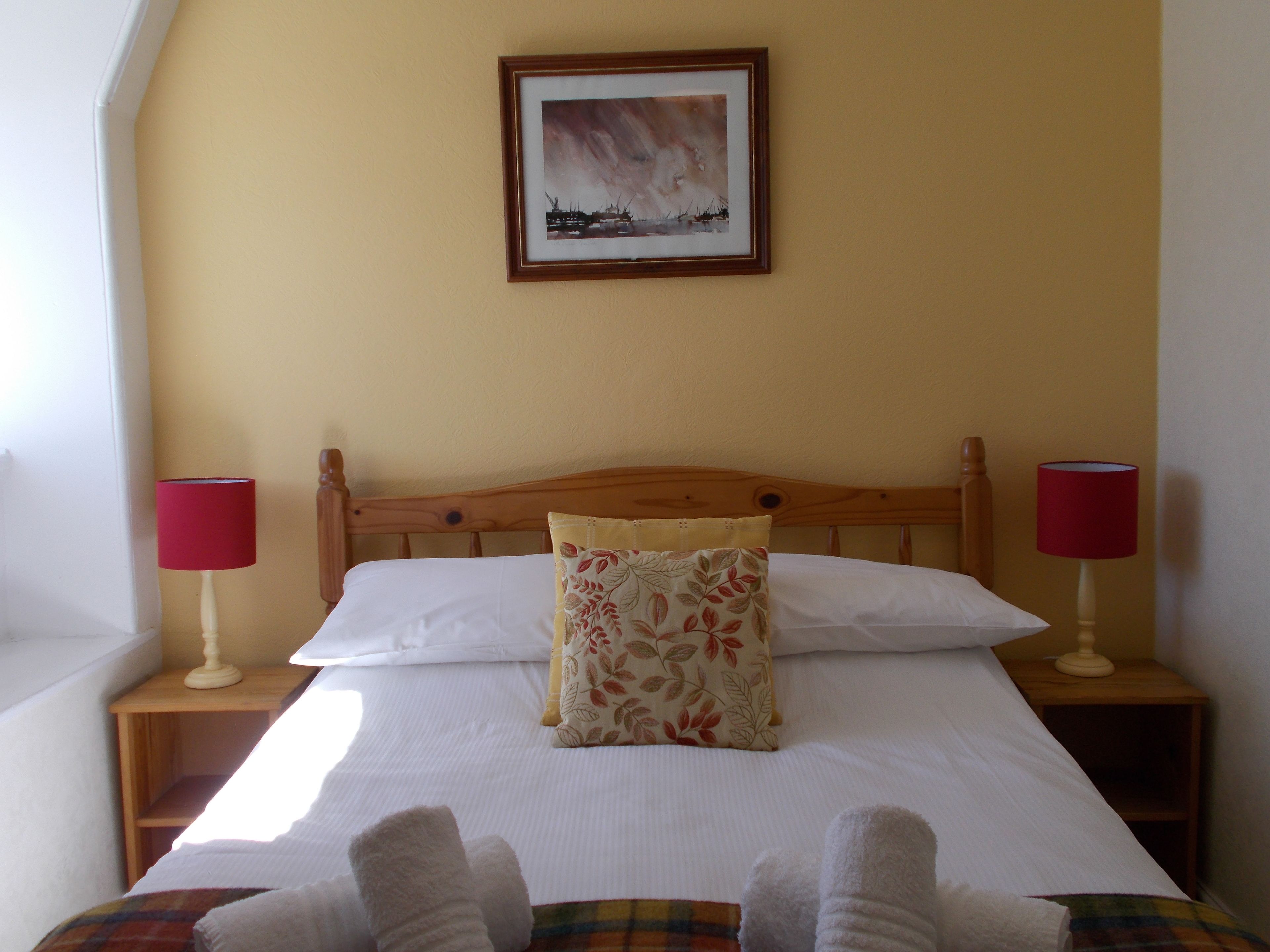A neatly made bed with white linens, a floral pillow, and two bedside lamps with red shades.