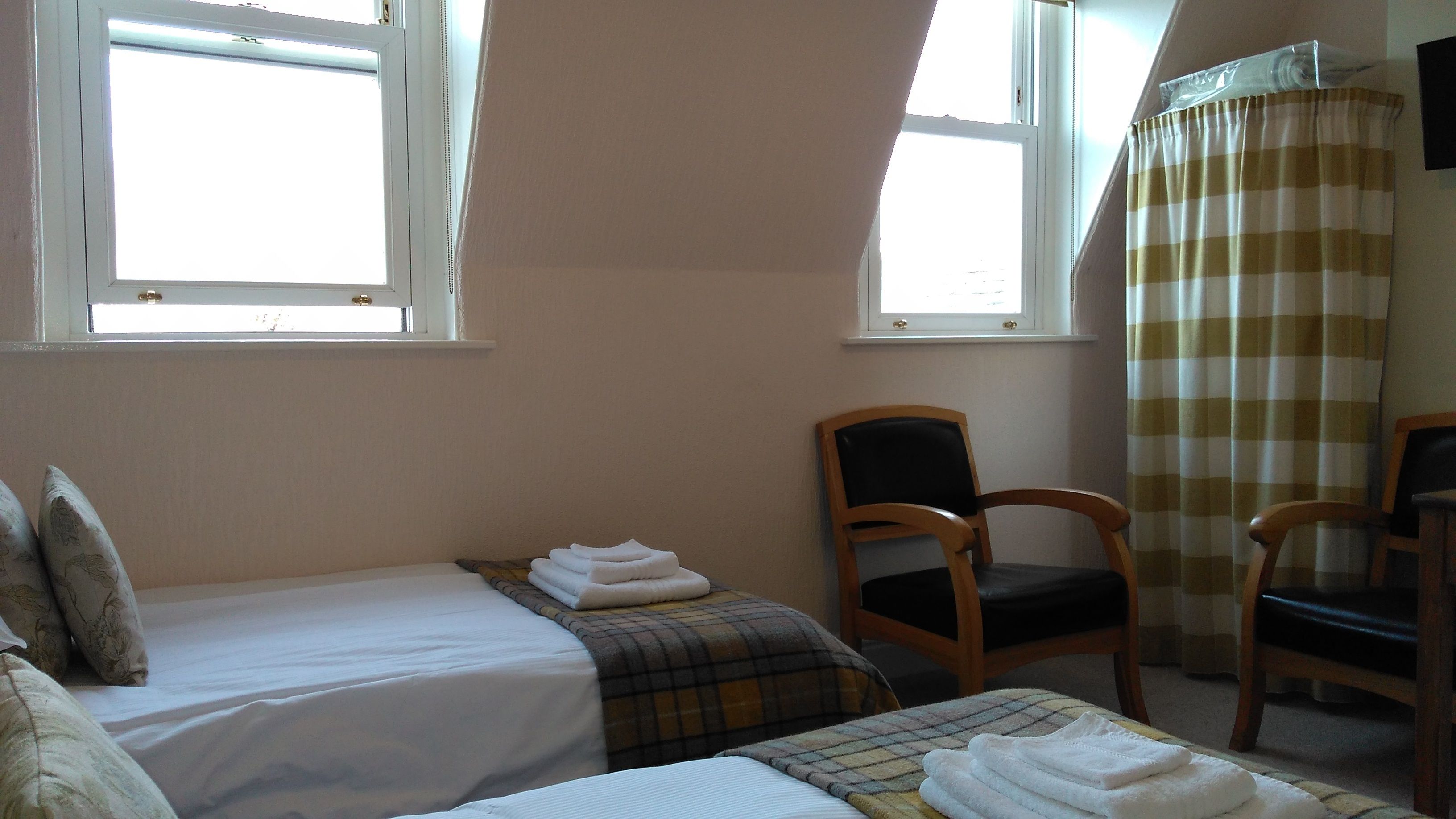 Une chambre avec deux lits, une chaise et une fenêtre avec des rideaux.