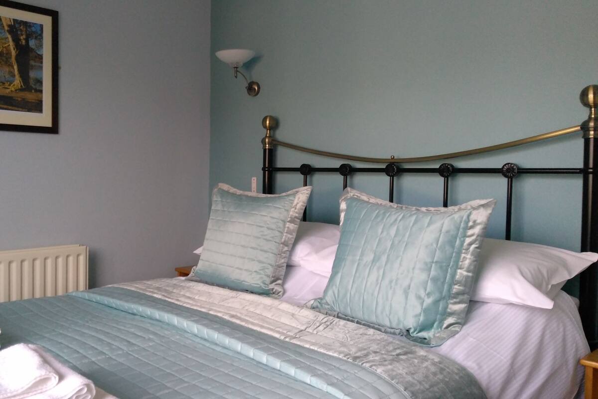 A bedroom with a bed, a radiator, a nightstand, and a framed picture on the wall.