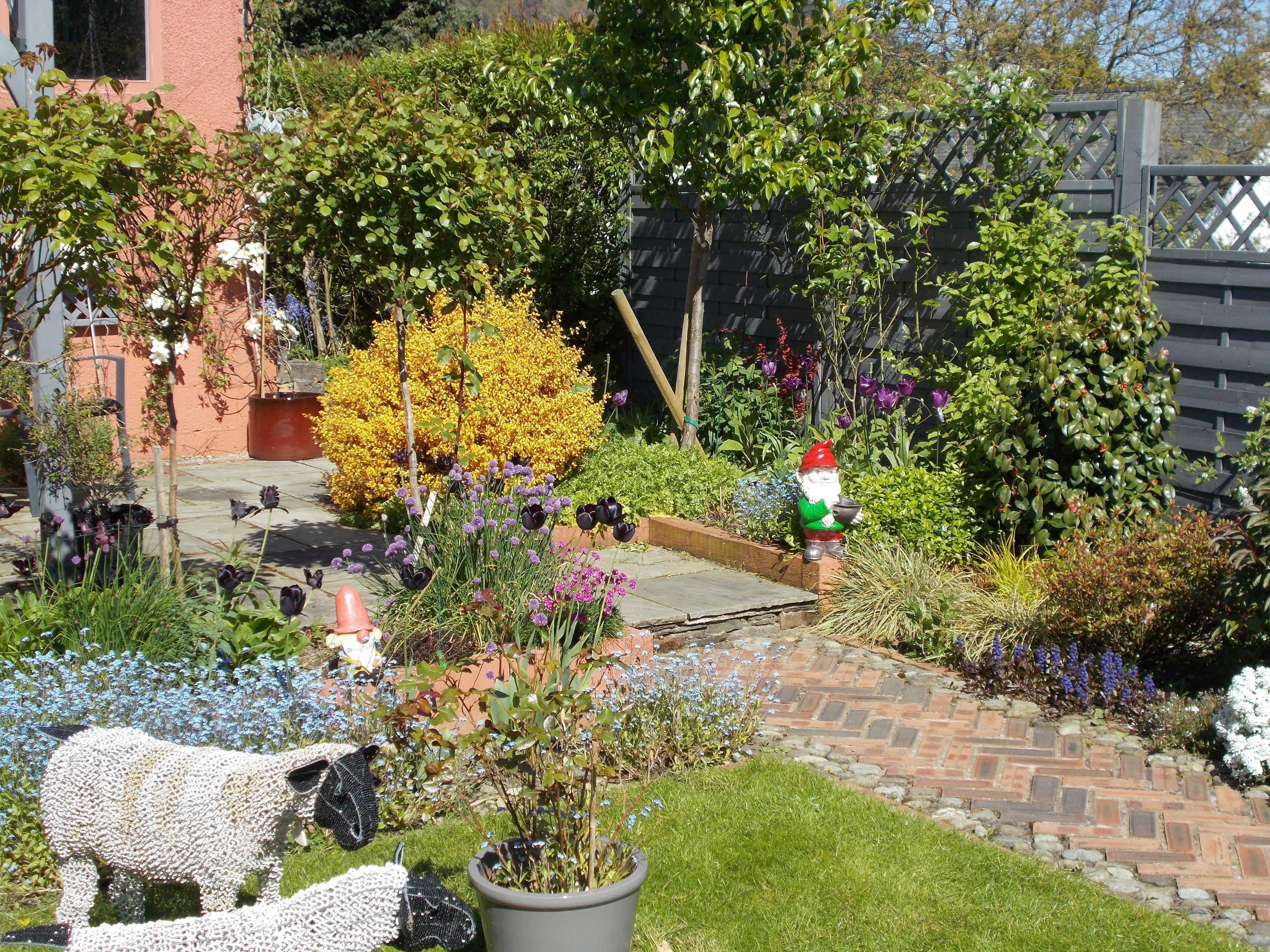 A garden with a gnome statue, a sheep sculpture, and various plants.