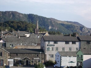 A hotel with a sign reading "Queens Hotel" in a town with buildings and a church spire in the background. - Swiss Court (Keswick)